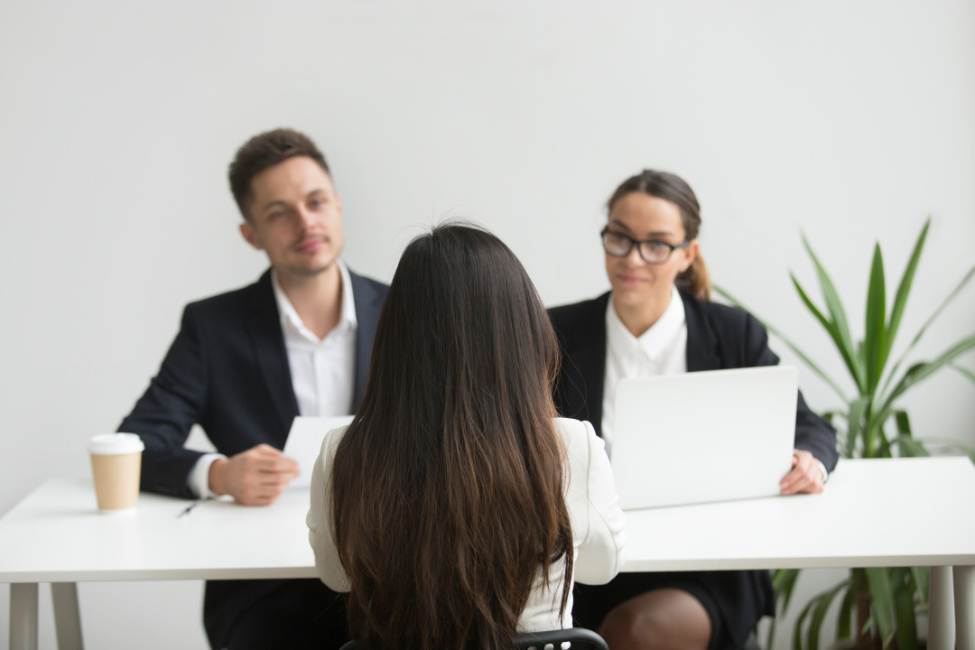 Back close up view of female applicant being interviewed by two HR managers reading her resume, checking data on laptop, asking questions for job position. Employment, hiring, first impression concept